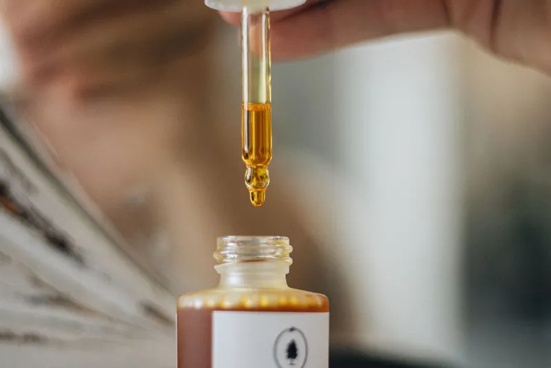 Pipette d'où perle une goutte de sérum doré, au-dessus de son flacon ouvert
