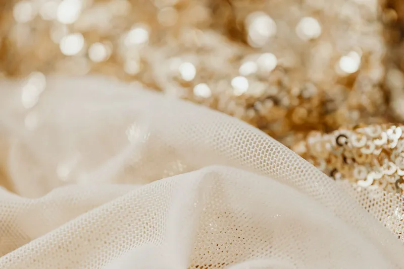Tissu doré couvert de sequins scintillants au-dessus d'un tulle ivoire froissé