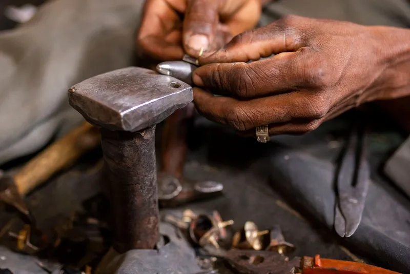 Mains d'artisan façonnant une bague sur une petite enclume, entre des pinces et des bagues en laiton inachevées