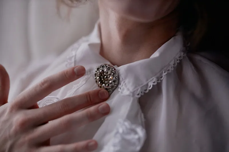 Broche ronde en métal à facettes épinglée au col en dentelle d'un chemisier blanc, effleurée par une main
