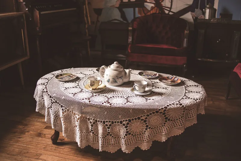 Service à thé en porcelaine fleurie sur une nappe ronde au crochet, dans un salon ancien au fauteuil de velours rouge