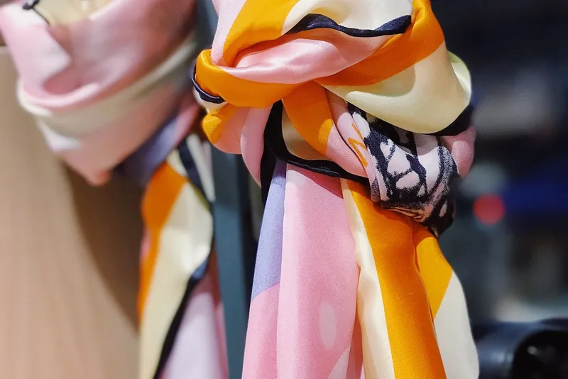 Foulard satiné imprimé de larges bandes rose, orange et crème cernées de bleu marine, noué en un nœud souple