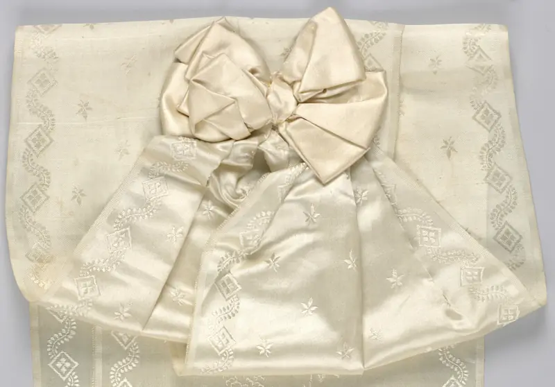 Un nœud de satin ivoire posé sur deux larges rubans de soie façonnée à motifs de fleurs, de losanges et de rinceaux